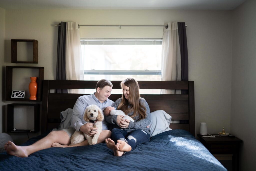 A family snuggles up on the master bed with their pups and newborn baby