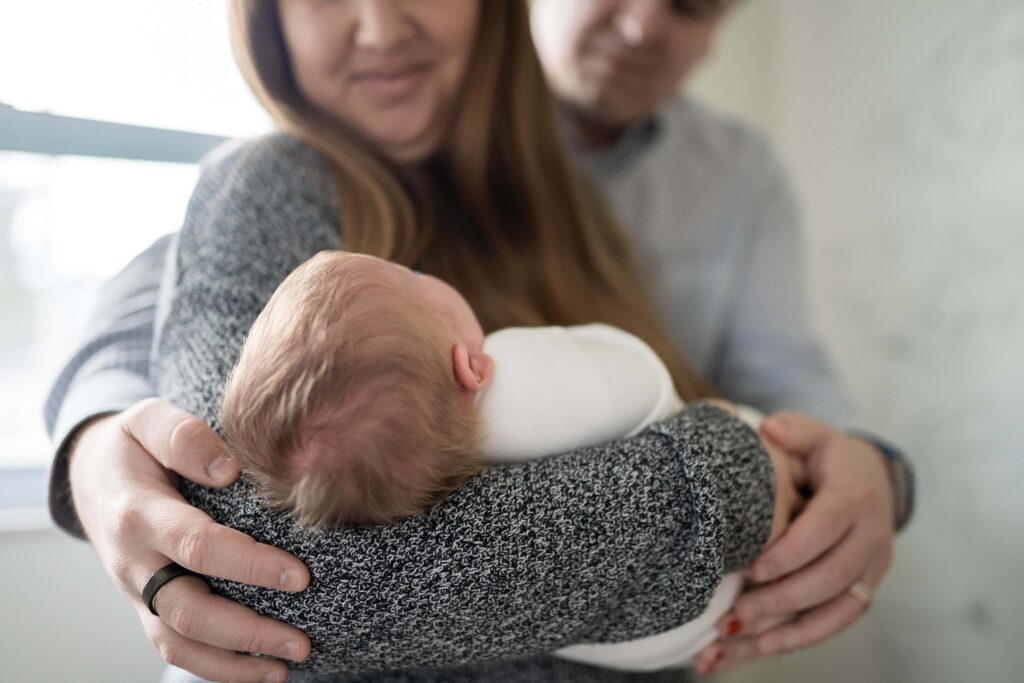 A baby is being cradled in her mom's arms while both parents look on