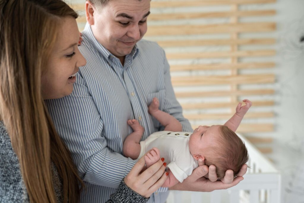 Mom and dad make faces at their newborn daughter in the nursery