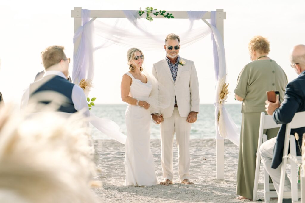 A bride and groom listen to mom talk during their ceremony on the beach