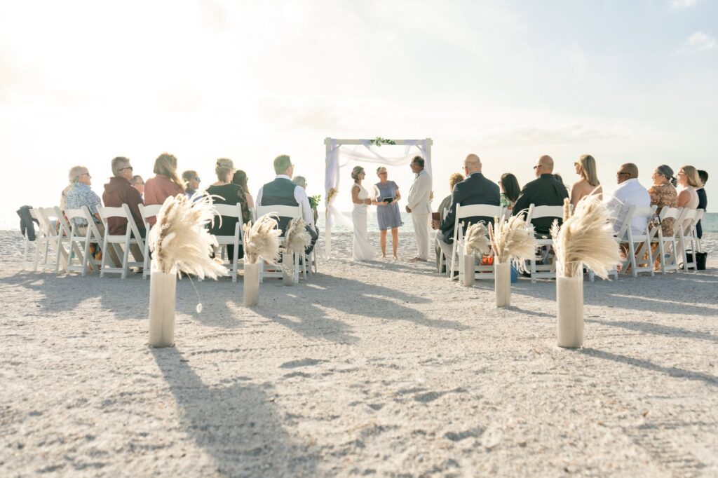 A beachy wedding setup with neutral florals and white chairs with an arch