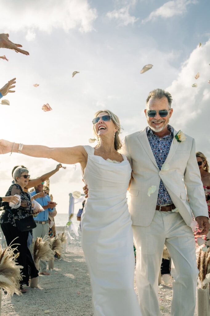 Joy radiates as a bride and groom walk down the aisle surrounded by friends and family throwing rose petals