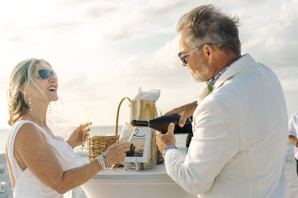 A groom pours his bride a glass of champagne as they prepare for toasts on the beach