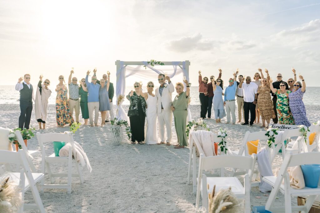 The entire wedding toasts to the bride and groom on the beach at their celebration
