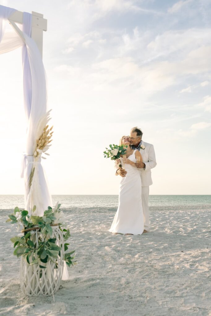 A post-wedding embrace on the beach behind their wedding arch