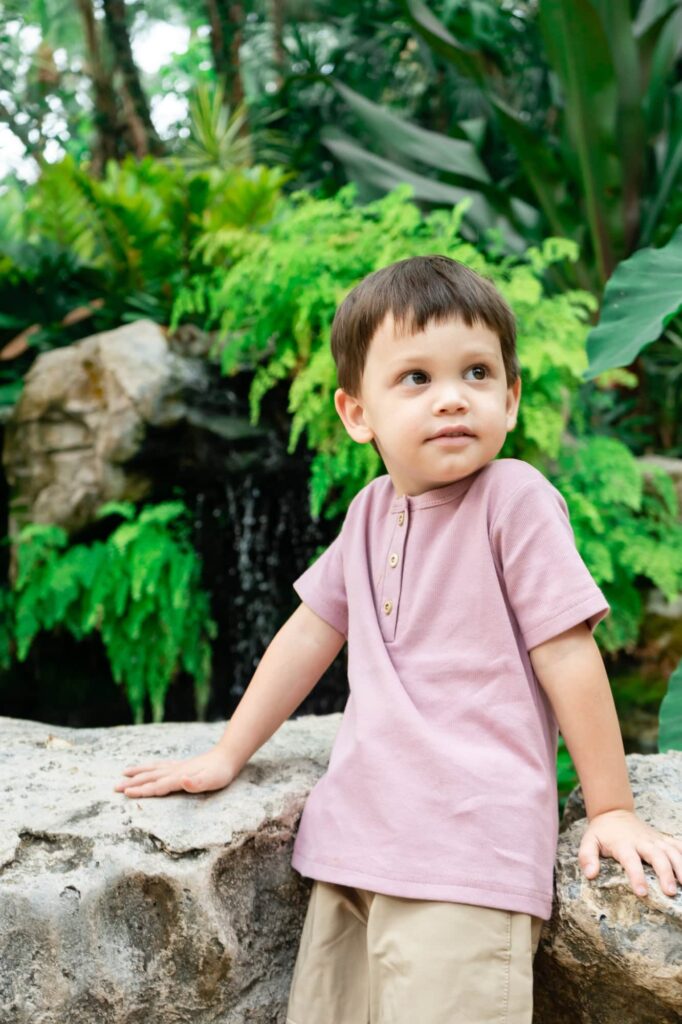 Young boy in a pink shirt sitting on a stone ledge near the waterfall at Sunken Gardens in St. Petersburg