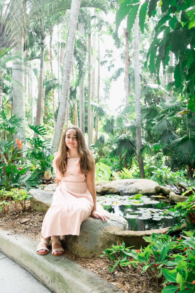 Girl in a light pink dress sitting on a rock by the pond at Sunken Gardens during family portraits