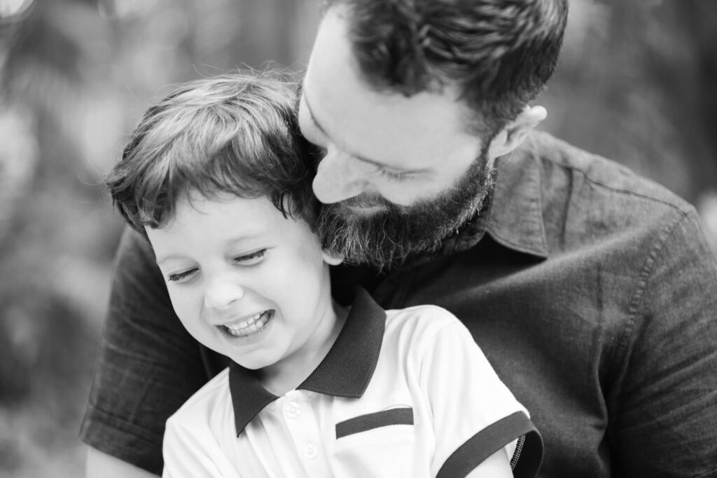 Dad cuddling and smiling with his young son during a candid family photo at Sunken Gardens
