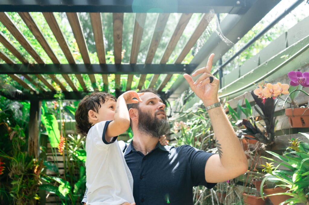 Father holding his son and pointing up while exploring the orchid house at Sunken Gardens in St. Petersburg