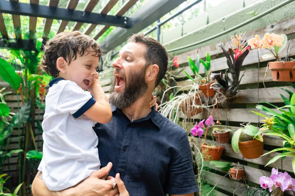 Dad and son laughing together in the orchid garden during their Sunken Gardens family session in St. Pete