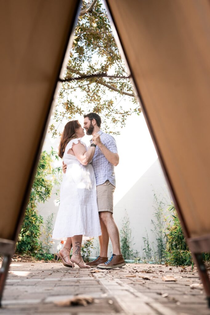 Playful moment of a couple dancing together framed between two beams outdoors in St Pete. A candid, natural engagement photo showing connection for couples who feel awkward posing.