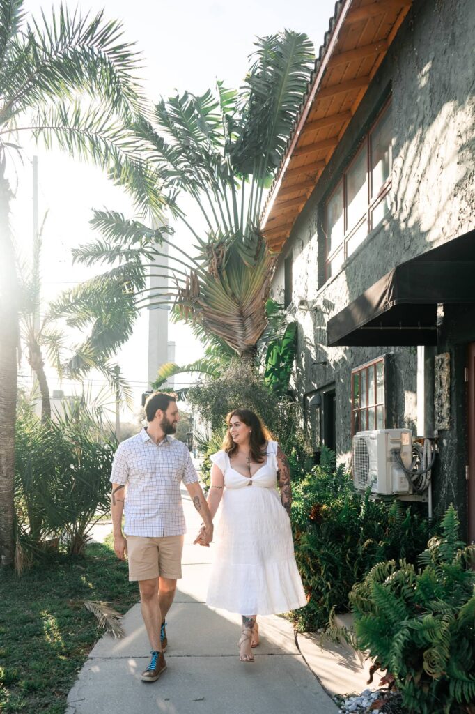 Couple walking hand in hand along a palm-lined street in downtown St Pete during their engagement session. A natural way to turn awkward photos into fun, candid memories.