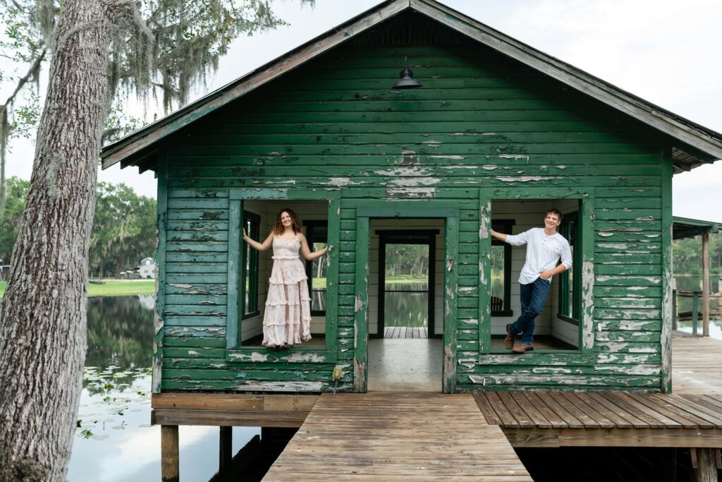 Couple posing in the windows of a rustic green boathouse during their St Pete engagement session. A creative and candid engagement photo idea for couples who don’t want stiff, awkward posing.