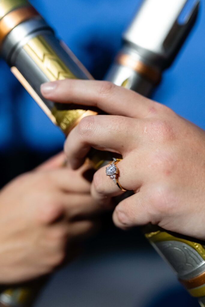 Close-up of a diamond engagement ring with hands holding lightsabers. A detailed and creative engagement photo idea for awkward couples who want something unique in St Pete.