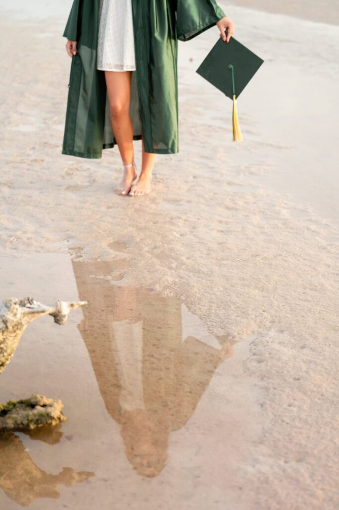 Creative senior portrait showing gown and cap reflected in shallow water