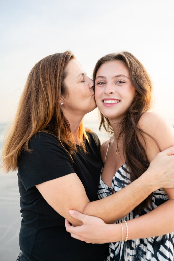 Candid beach photo of mom kissing her daughter on the cheek during senior session