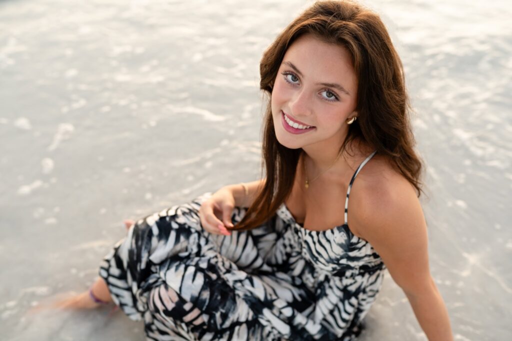 Senior portrait of teen sitting in shallow water at Fort De Soto, smiling toward the camera