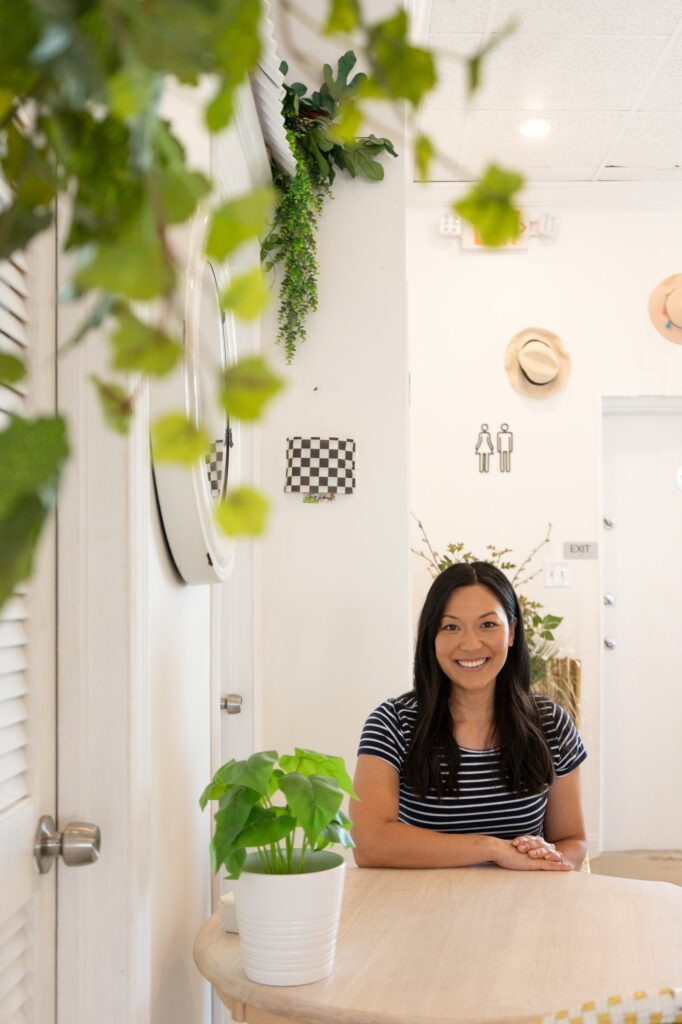 Audra, Tampa wedding planner and owner of Til Death Weddings & Design, smiles while sitting at a cozy table surrounded by greenery, photographed by Erin Vestal Photography.