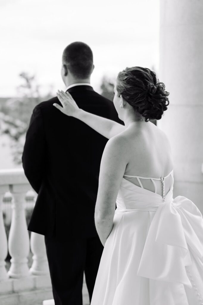 Bride gently placing her hand on groom’s shoulder before first look, captured on balcony by Tampa Bay wedding photographer Erin Vestal.
