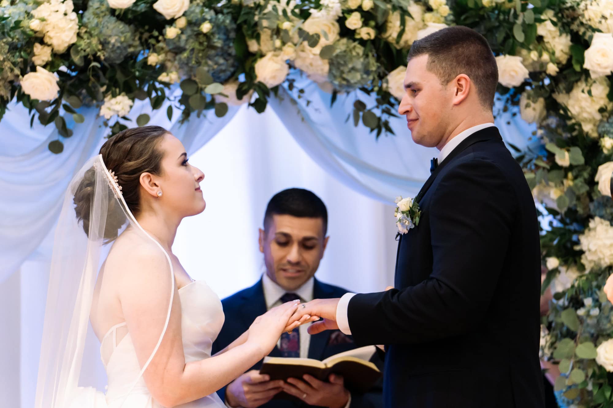 Bride and groom exchanging rings beneath floral arch during Tampa Bay wedding ceremony, captured by Erin Vestal Photography.