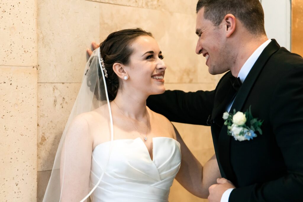Bride and groom smiling and laughing together against marble wall during candid wedding portrait captured by Erin Vestal Photography.