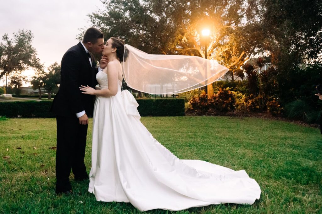 Bride and groom kissing outdoors at sunset with flowing veil and glowing streetlight, captured by Erin Vestal Photography.