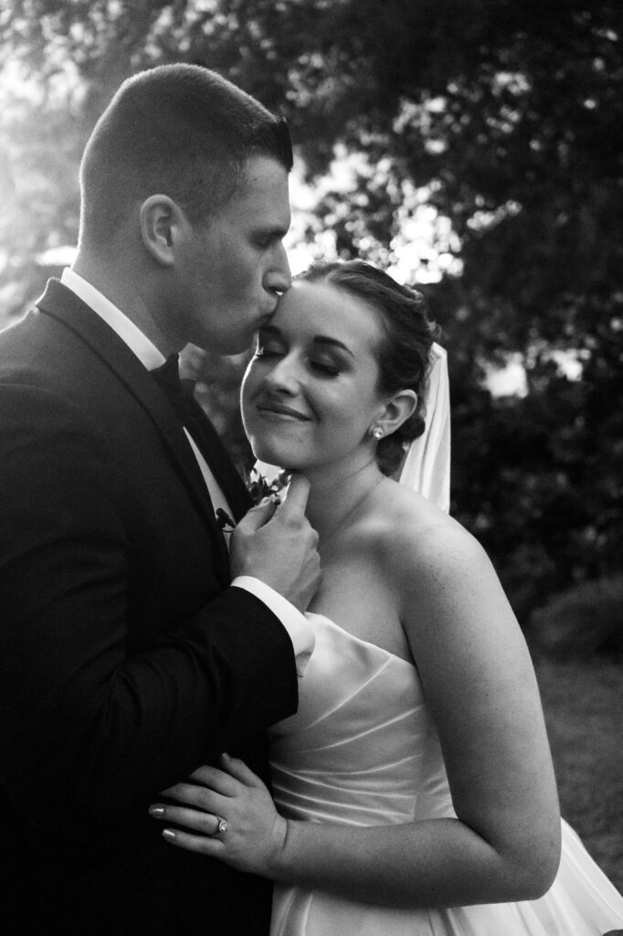 Groom kissing bride’s forehead as she smiles softly during golden hour portraits at Florida wedding, photographed by Erin Vestal.