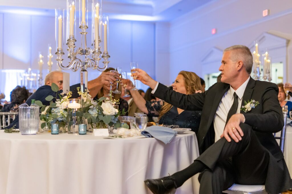 Family and friends raising glasses in toast under elegant candlelight at wedding reception, photographed by Erin Vestal.