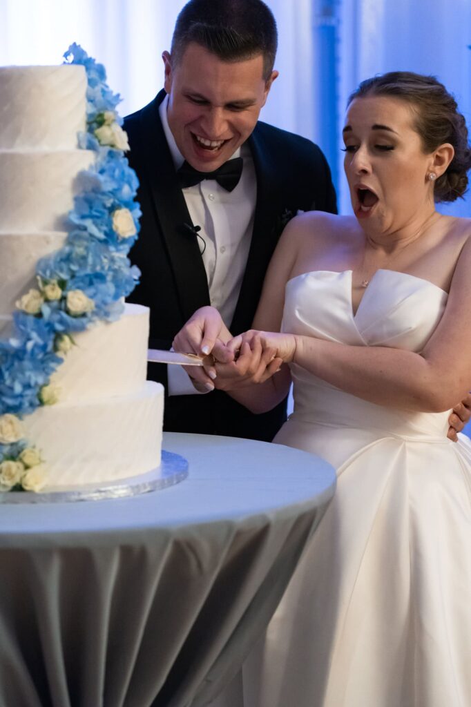 Bride and groom cutting tiered wedding cake together and laughing joyfully during reception, captured by Erin Vestal Photography.
