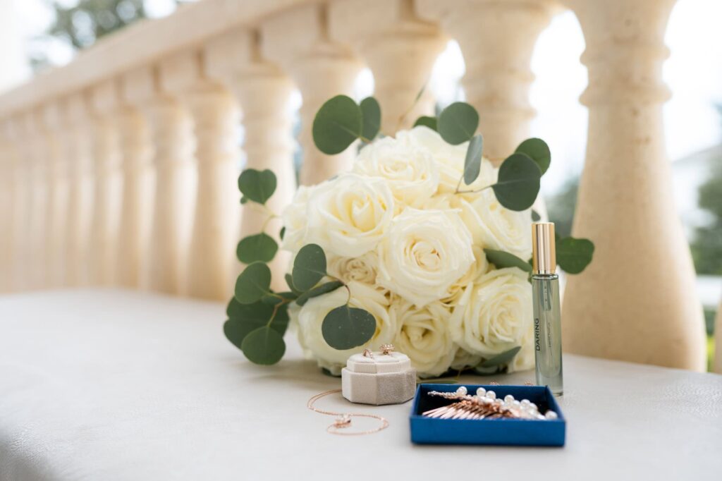 Bridal bouquet of white roses, eucalyptus, and gold perfume bottle displayed on stone terrace, photographed by St. Pete wedding photographer Erin Vestal.