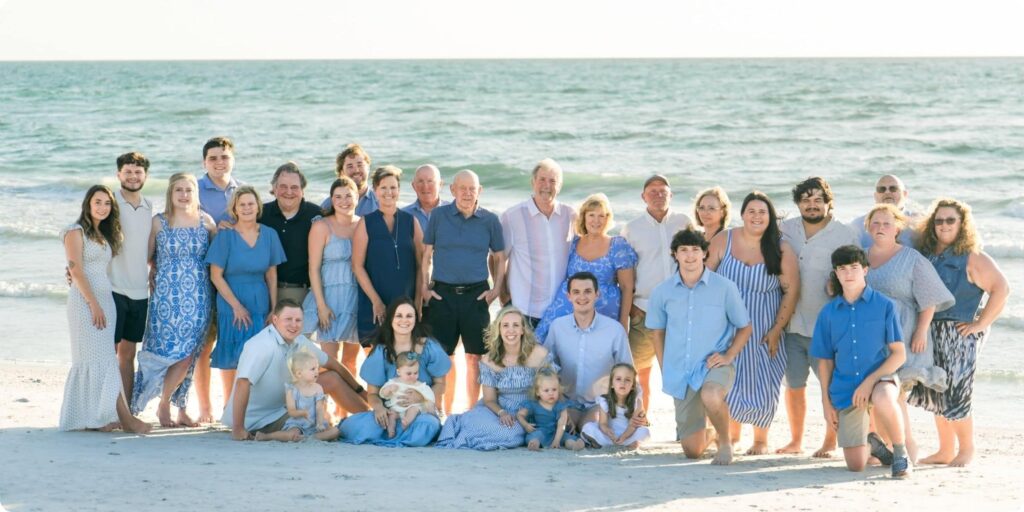 Extended family in light blue and white outfits gathered on the beach at sunset during a joyful holiday family session in St. Pete Beach, FL.