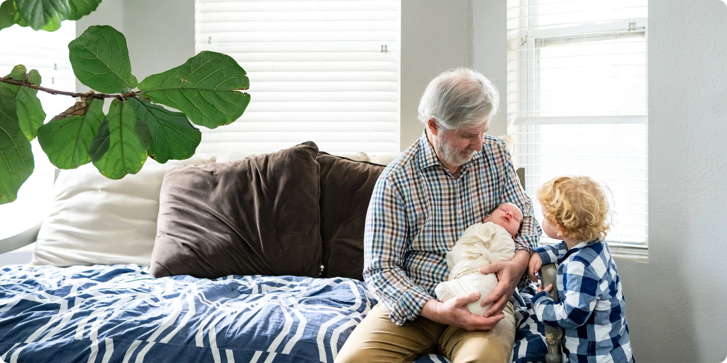 Grandfather holding newborn while curious toddler looks on, photographed in family home — in-home newborn photography Pinellas County