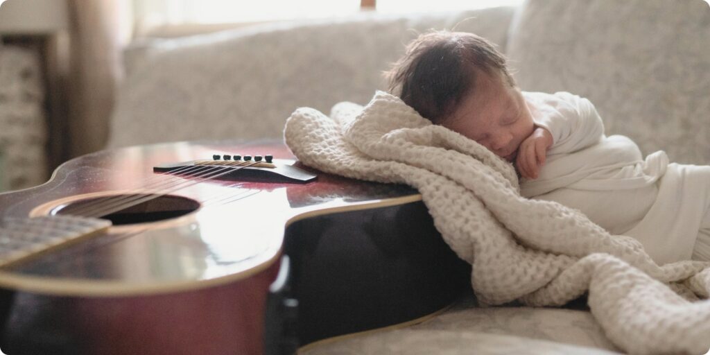 Newborn baby sleeping against acoustic guitar, wrapped in cream knit blanket — sentimental heirloom newborn photography St. Petersburg FL