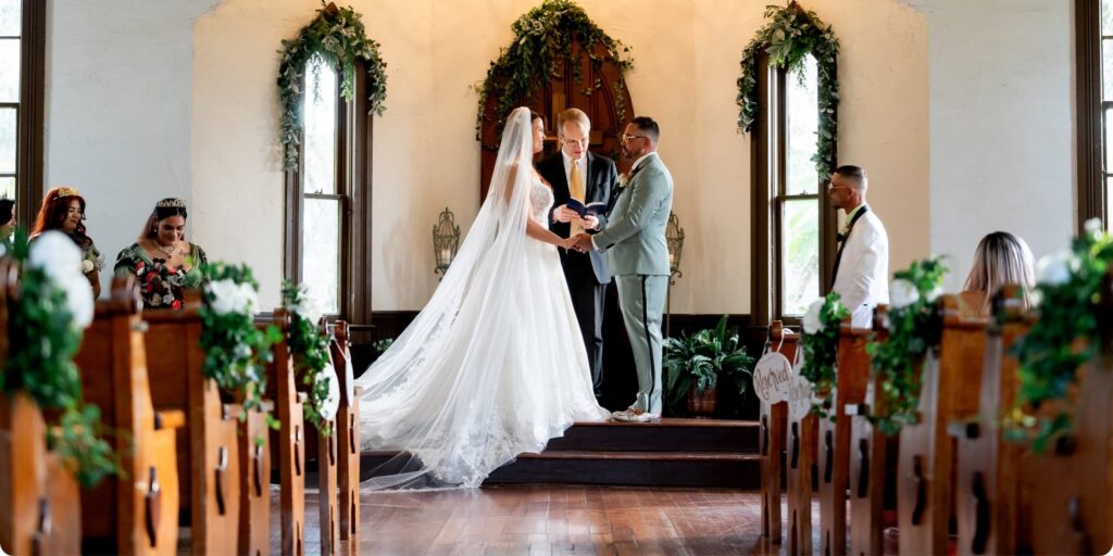 Bride and groom exchanging vows at Historic Andrews Memorial Chapel in Dunedin Florida, surrounded by wooden pews and tall windows with natural light