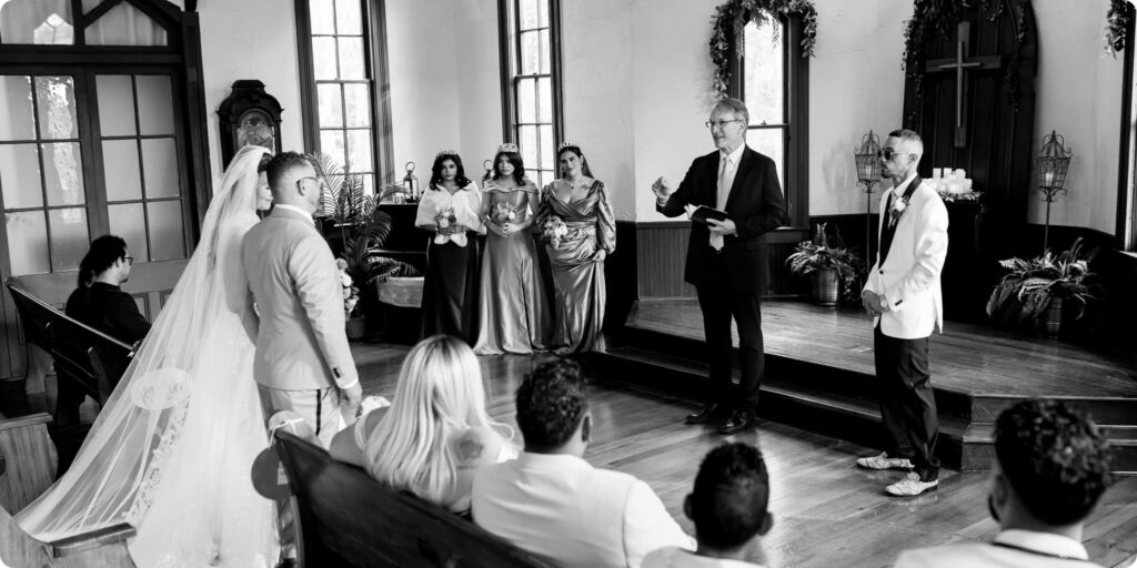 Wide angle black and white photo of intimate wedding ceremony at Historic Andrews Memorial Chapel in Dunedin Florida with bridesmaids and small guest count