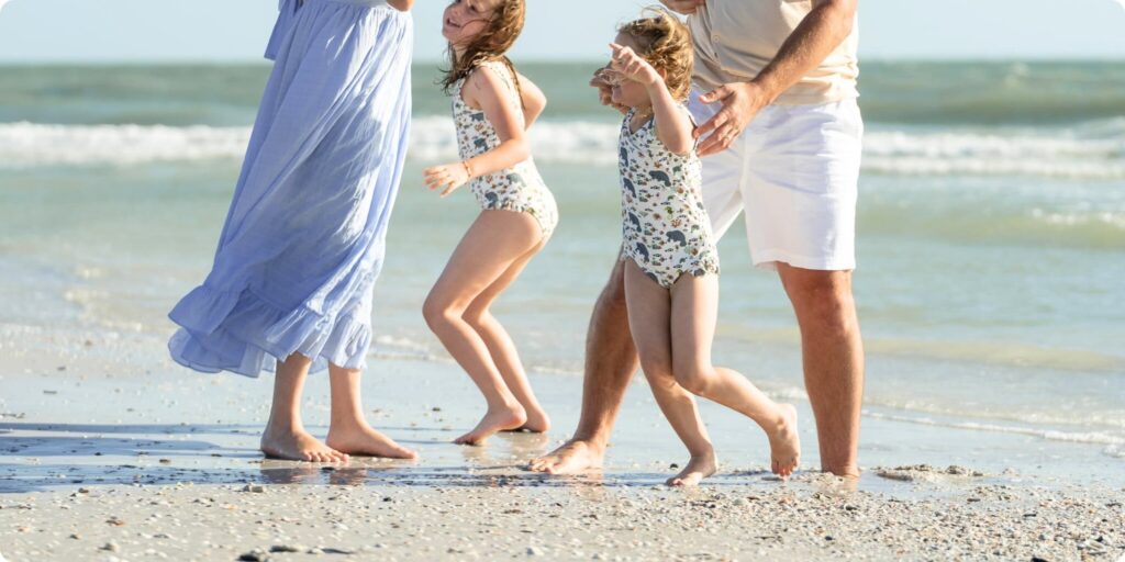 Family walking along the shoreline at St. Pete Beach with two daughters in matching swimsuits during a spring break family session