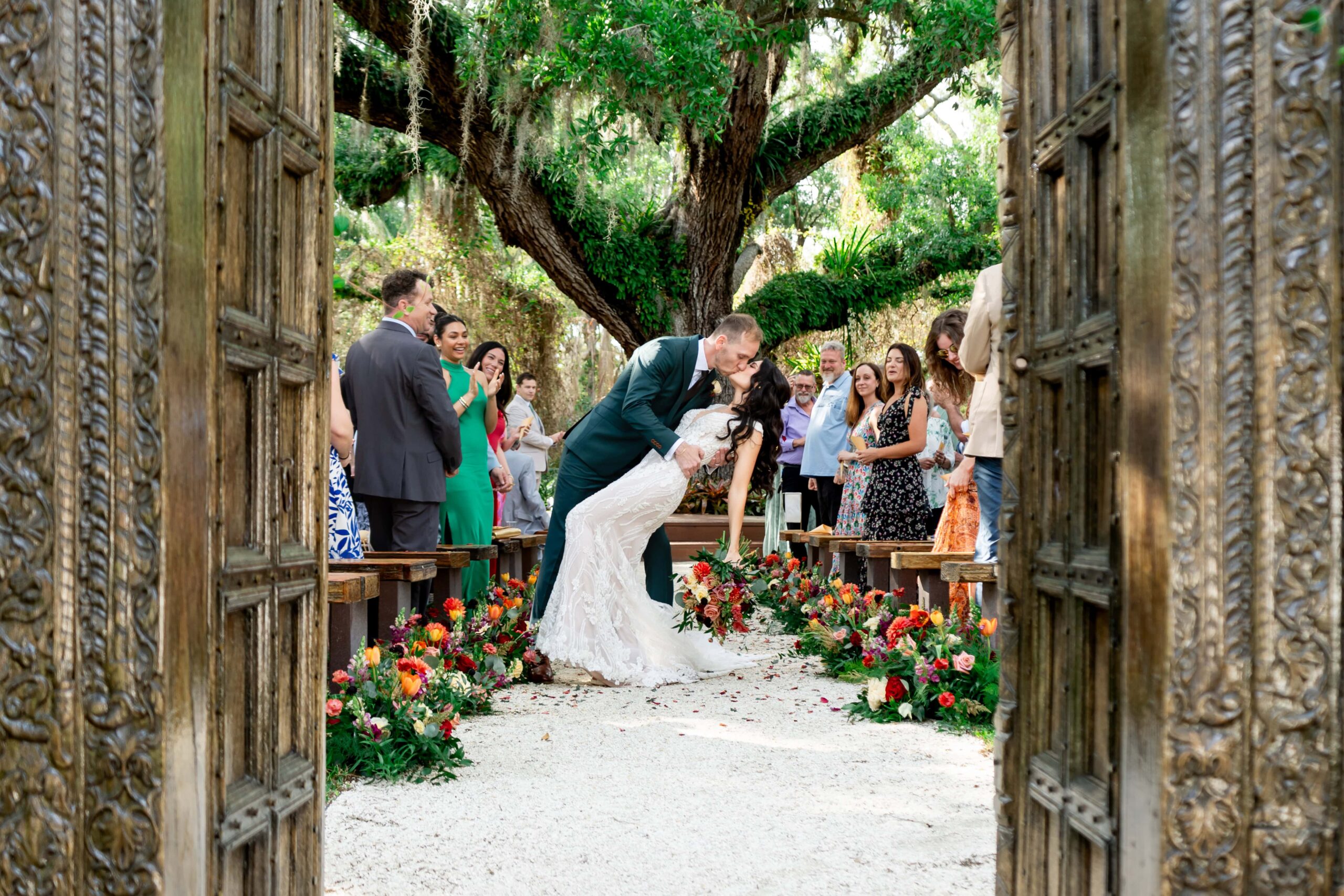 A couple kisses in the aisle after their wedding ceremony while surrounded by family and friends