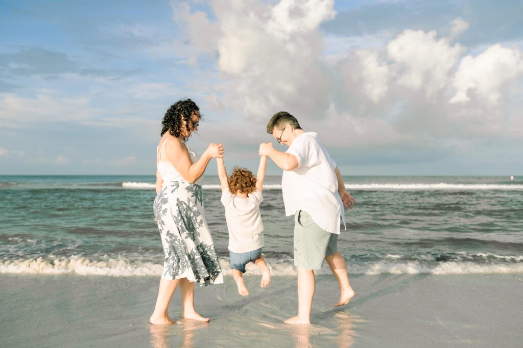 Two moms swing their son into the waves on the beach at Fort DeSoto in the morning sunshine